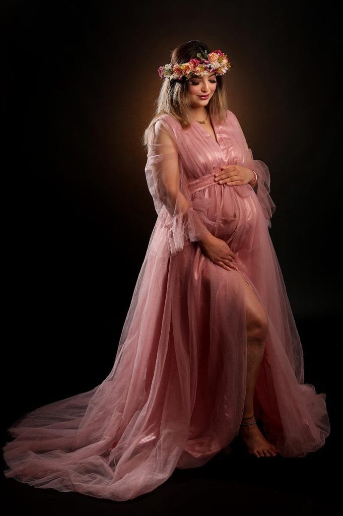 Beautiful expectant mother in pink tulle gown and floral crown poses for a dramatic Maternity Photoshoot.