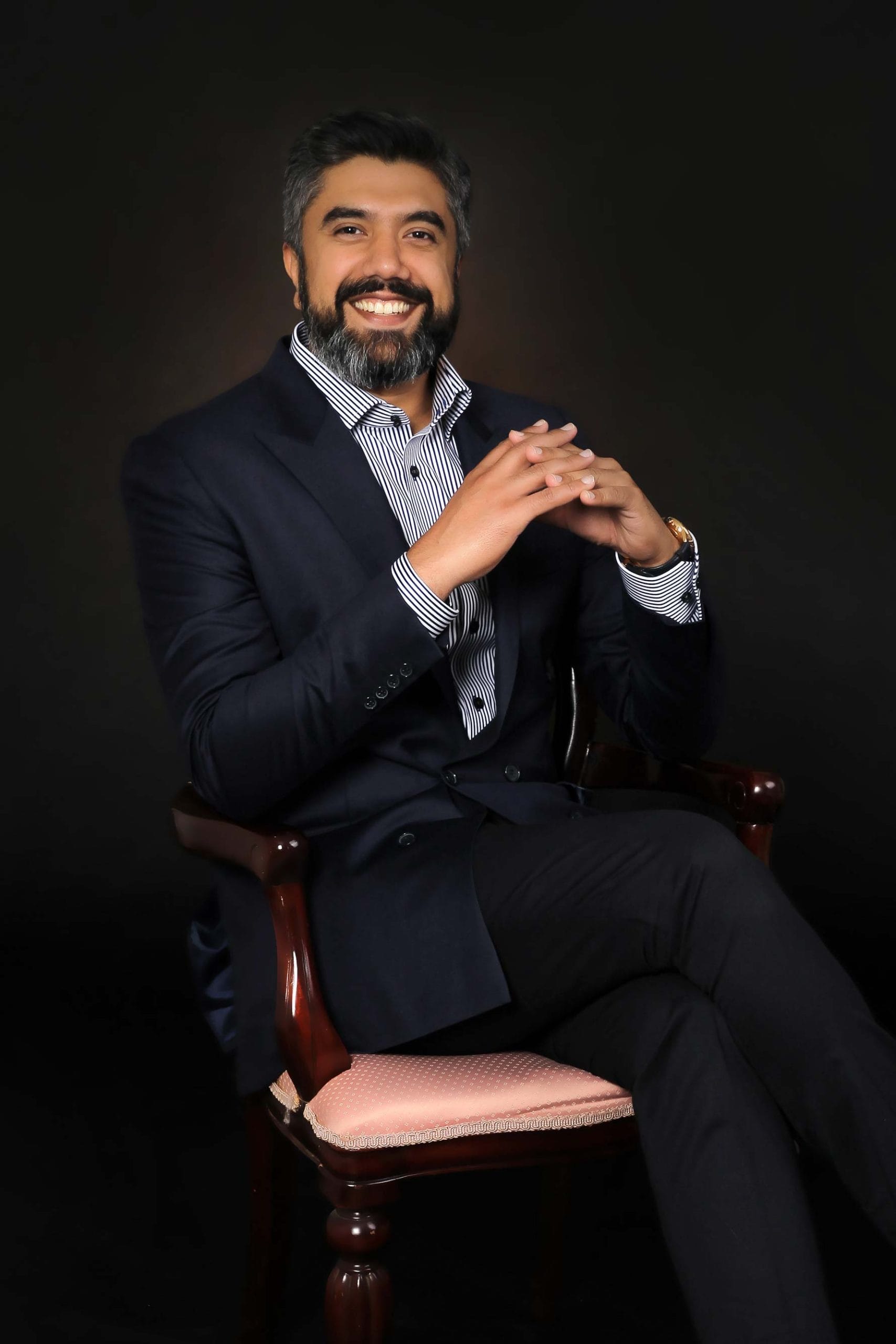 Confident man in a suit with a striped shirt smiling while sitting on an elegant chair during a corporate photo session