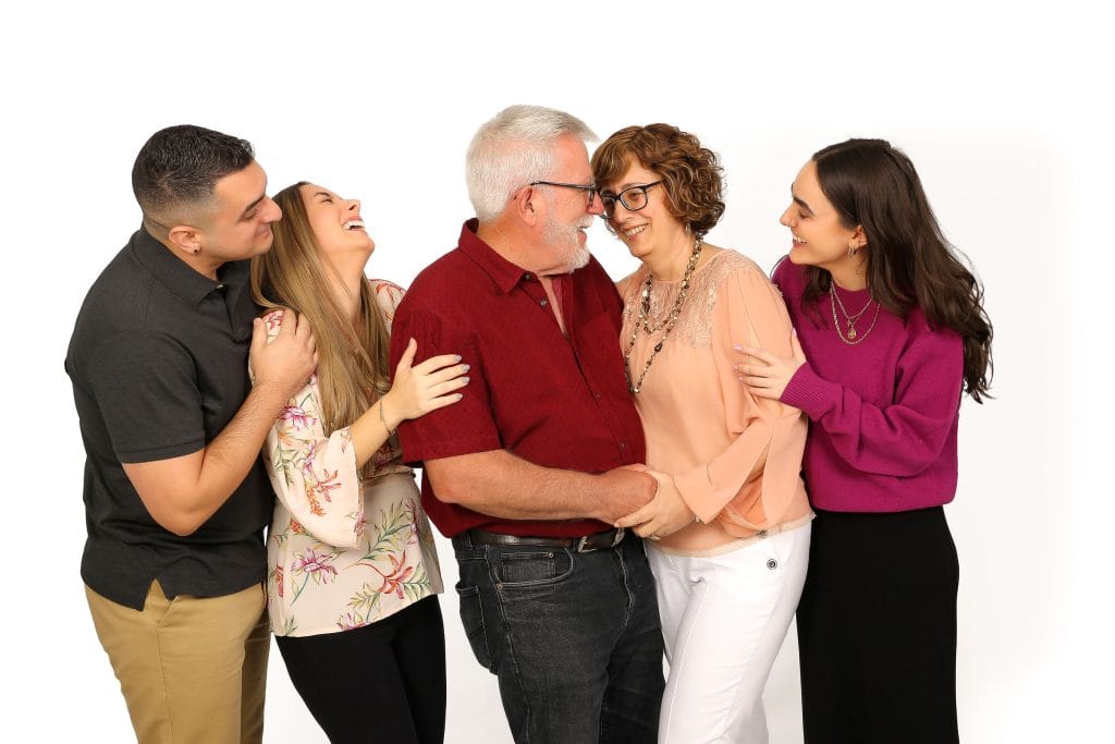 Cheerful family of five, including parents and three adult children, smiling and laughing together in a bright white studio