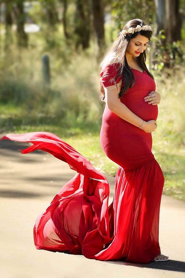 Pregnant woman in a red mermaid gown with a long flowing train outdoors for a Maternity Photoshoot.