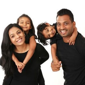 Smiling family of four posing together, with two children playfully hugging their parents against a white studio background