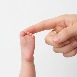 A close-up of an adult's hand with a gold ring gently touching a newborn baby's tiny toes, highlighting a tender moment.